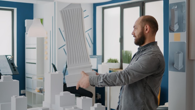 Mannarchitekt, der Gebäudemodell und Maquette analysiert, um städtisches Eigentum zu entwerfen. Architekturarbeiter, der Blaudruckpläne und Konstruktionspläne für ein modernes Strukturprojekt entwirft.