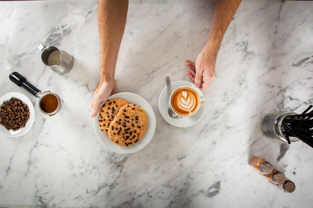 Mannhände mit Plätzchen und einem Cappuccino