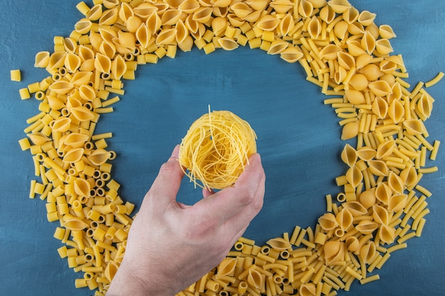 Kostenloses Foto mannhand, die ungekochte nestnudeln auf einem dunkelblauen hintergrund hält.