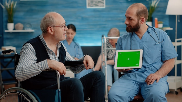 Mannkrankenschwester und alter Patient, der den grünen Bildschirm auf dem Tablet betrachtet