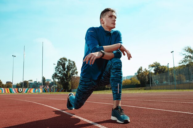 Mannläufer, der Beine streckt, bereitet sich auf Lauftraining auf Stadionbahnen vor, die Aufwärmen tun
