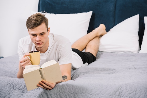 Kostenloses Foto mannlesebuch, das auf bett liegt