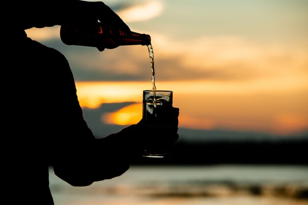 Mannschattenbild, das ein Bier während eines Sonnenuntergangs hält