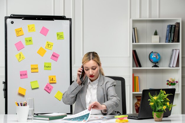 Marketing ziemlich süße junge Geschäftsfrau im grauen Anzug im Büro, die Diagramme am Telefon betrachtet