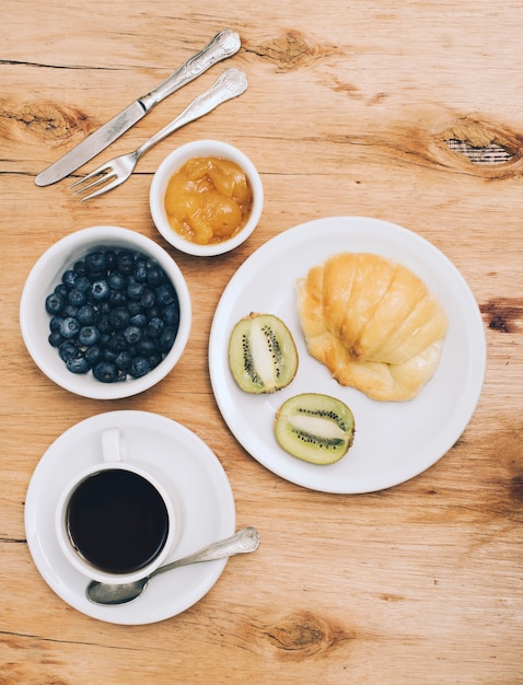 Marmelade; Blaubeeren; Kiwi; Brot und Kaffeetasse auf hölzernen strukturierten Hintergrund