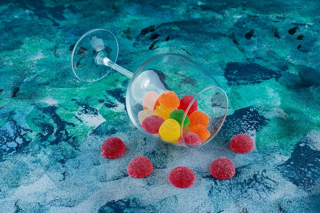 Kostenloses Foto marmeladenbonbons im umgestürzten glas, auf dem blauen hintergrund.