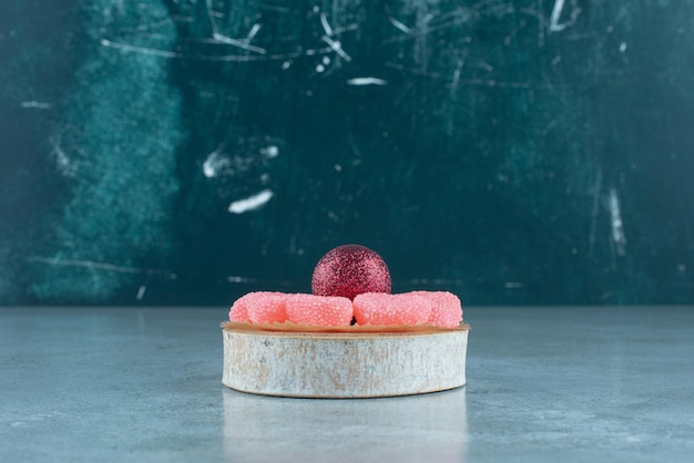 Marmeladenring um eine Weihnachtskugel auf einem Stück Holz auf Blau.