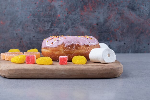 Marmeladenstücke, Marshmallows und ein Donut auf einem Holzbrett auf Marmoroberfläche