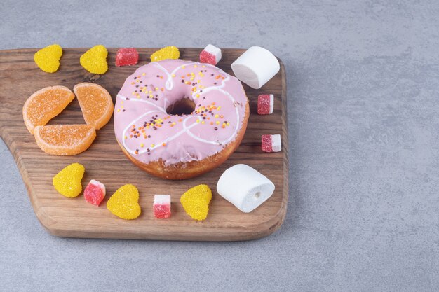 Marshmallows, Marmeladen und ein Donut auf einem Holzbrett auf Marmoroberfläche