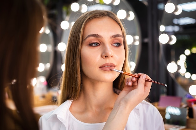 Maskenbildner, der Lippenstift auf Frau mit Bürste anwendet