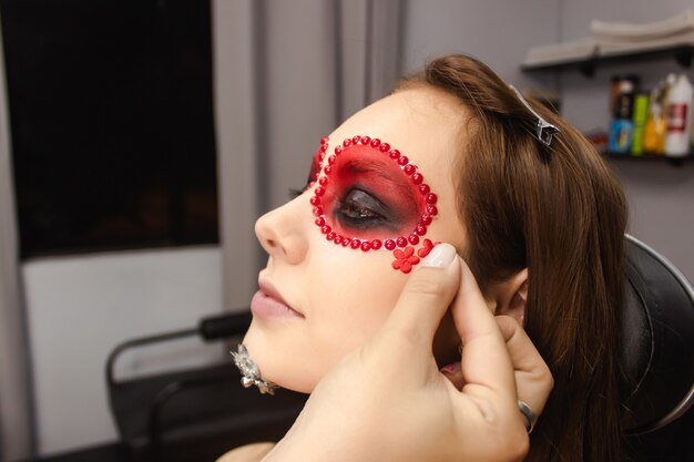 Maskenbildner klebt accessoires auf das gesicht eines schönen mädchens dia de los muertos make-up Premium Fotos