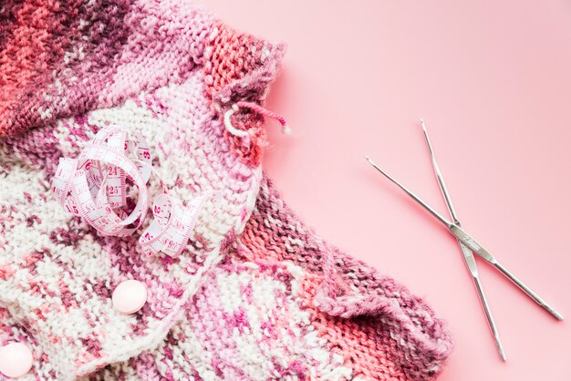 Maßband mit stricken Häkeln und Nadeln auf rosa Hintergrund