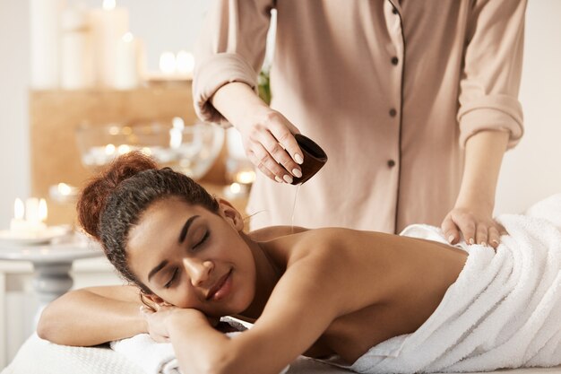 Masseur gießt Öl, das Massage für schöne afrikanische Frau im Spa-Salon tut.