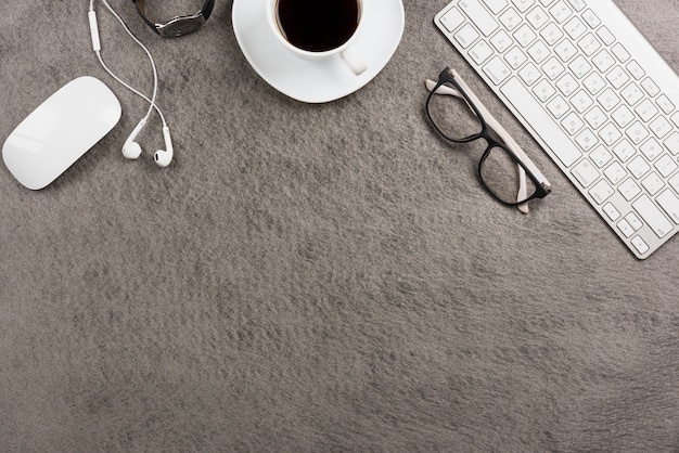 Maus; Tastatur; Kaffeetasse; Ohrtelefon; Armbanduhr auf grauem Hintergrund
