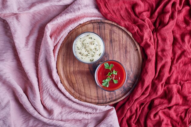 Mayonnaise und Ketchup in Glasbechern auf einer Holzplatte.