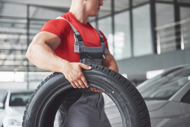 Mechaniker, der einen Reifenreifen in der Reparaturwerkstatt hält. Austausch von Winter- und Sommerreifen.