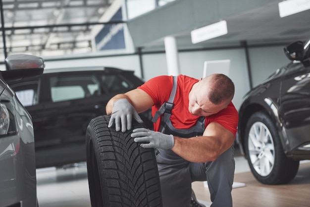 Mechaniker, der einen Reifenreifen in der Reparaturwerkstatt hält. Austausch von Winter- und Sommerreifen.