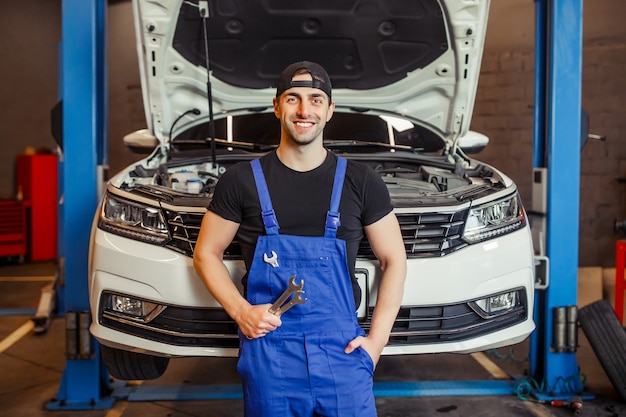 Kostenloses Foto mechaniker in uniform, der schraubenschlüssel im auto-service-center hält und in die kamera lächelt