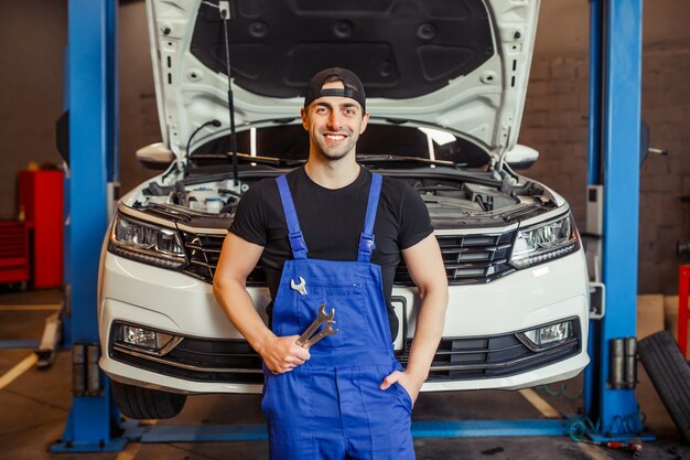 Mechaniker in Uniform, der Schraubenschlüssel im Auto-Service-Center hält und in die Kamera lächelt