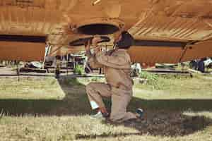 Kostenloses Foto mechaniker in uniform und fliegendem helm reparieren retro-militärflugzeug in einem freilichtmuseum.