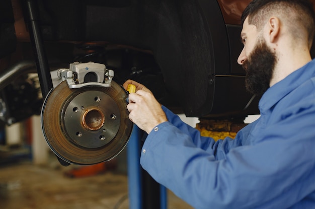 Mechaniker mit einem Werkzeug. Rad in Händen eines Mechanikers. Blaue Arbeitskleidung.