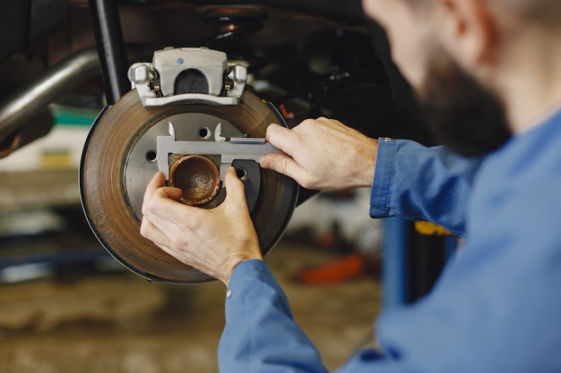 Mechaniker mit einem Werkzeug. Rad in Händen eines Mechanikers. Blaue Arbeitskleidung.