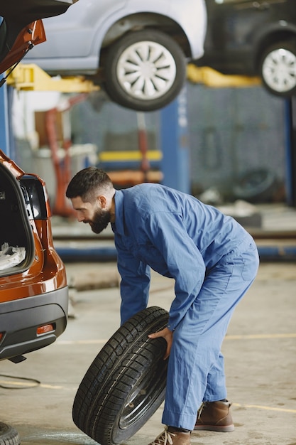 Mechaniker mit einem Werkzeug. Rad in Händen eines Mechanikers. Blaue Arbeitskleidung.