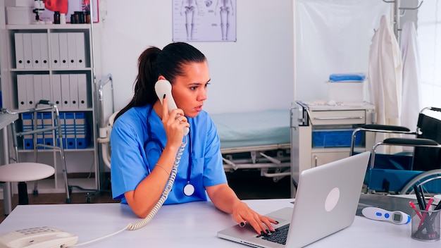 Medizinische empfangsdame, die mit dem patienten am telefon vom krankenhausüberprüfungstermin spricht. arzt im gesundheitswesen in medizinuniform, arzthelferin, die bei der telemedizinischen kommunikation hilft