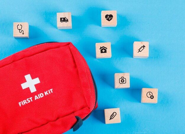 Medizinisches Konzept mit Holzklötzen mit Symbolen, Erste-Hilfe-Tasche auf blauem Tisch flach legen.