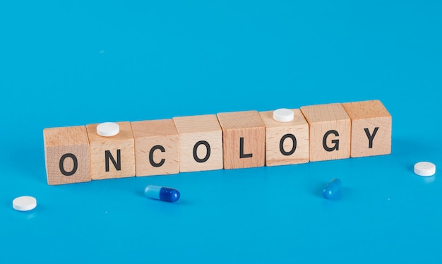 Medizinisches Konzept mit medizinischen Pillen, Onkologiewort auf hölzernen Würfeln auf der hohen Winkelansicht der blauen Tabelle.