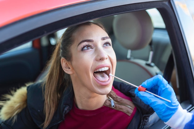 Medizinisches Personal, das eine Drive-Thru-COVID19-Prüfung durchführt, bei der eine Probe eines Nasenabstrichs von einer Patientin durch ein Autofenster genommen wird