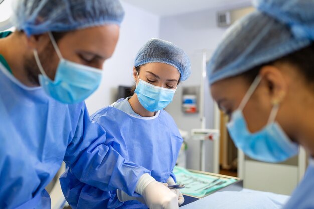 Medizinisches Team, das chirurgische Eingriffe in einem hellen, modernen Operationssaal durchführt Gruppe von Chirurgen bei der Arbeit im Operationssaal, blau getönt Medizinisches Team, das die Operation durchführt