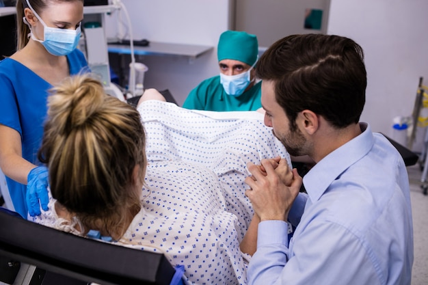 Medizinisches Team, das schwangere Frau während der Entbindung untersucht, während Mann ihre Hand hält