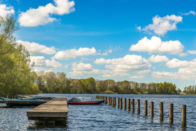 Meer mit Booten in der Nähe des Docks und grünen Bäumen in der Ferne unter einem blauen Himmel