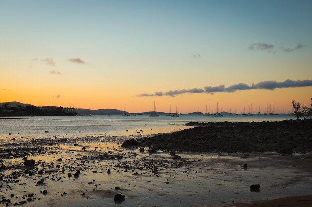 Meer mit Schiffen, umgeben von Strand und Hügeln während des Sonnenuntergangs am Abend