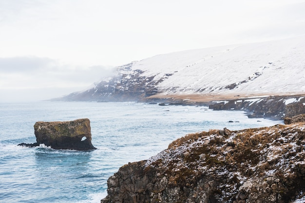 Meer umgeben von Hügeln, die mit Schnee und Nebel bedeckt sind, unter einem bewölkten Himmel in Island