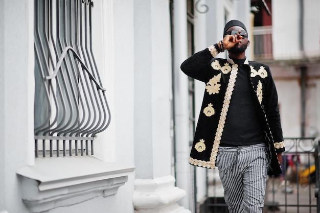 Mega stylischer afrikanischer Mann in traditioneller Jackenpose Modischer schwarzer Typ mit Hut und Sonnenbrille mit Zigarre in der Hand