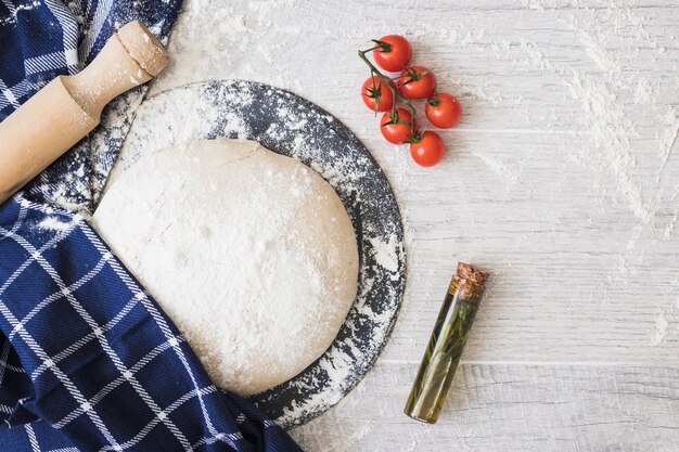 Mehl bestäubt auf Teigbrot; Kirschtomaten; Rosmarin und Nudelhölzer auf Holzbrett