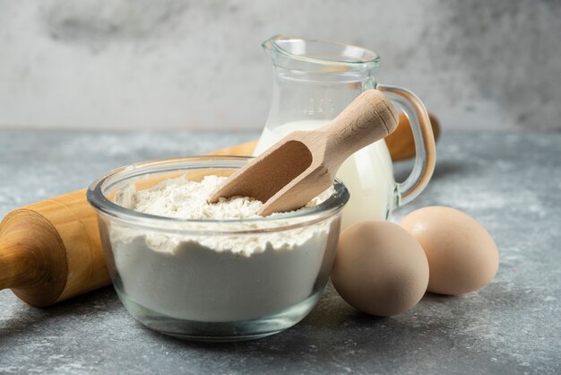 Mehl, Eier, Milch und Nudelholz auf Marmor.