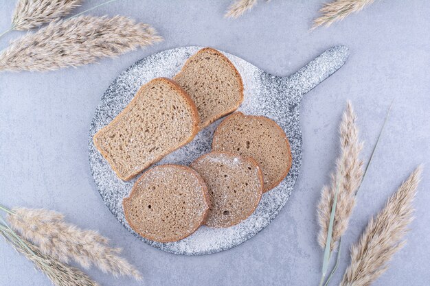 Mehlbedecktes Brett mit Brotscheiben neben Federgrasstielen auf Marmoroberfläche