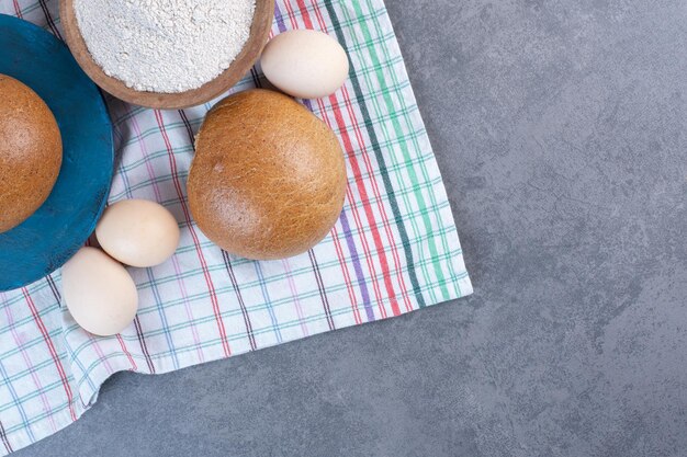 Mehlschüssel, Eier und Brötchen auf einem Handtuch auf Marmorhintergrund. Foto in hoher Qualität