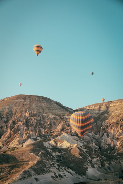 Mehrere bunte Heißluftballons schweben über Bergen