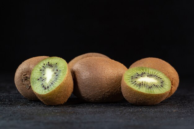 Mehrere frische reife saftige weiche Halbschnitte der braunen Kiwis isoliert auf dunklem Schreibtisch