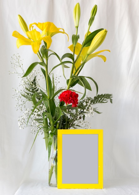 Mehrfarbige Blumen im Blumenvase mit leerem leerem Fotorahmen vor weißem Vorhang