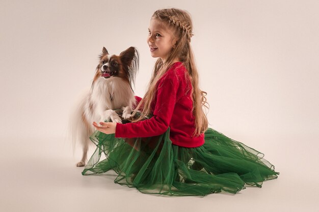 Mein kleiner Freund. Studioaufnahme eines kleinen gähnenden Welpen Papillon auf grauem Hintergrund mit kleinem jugendlich Mädchen im Studio. Liebe zum Tierkonzept. Junges kaukasisches Model.