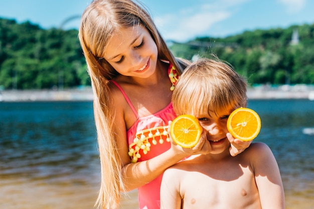 Meine lieben Kinder spielen mit Orangenscheiben am Strand