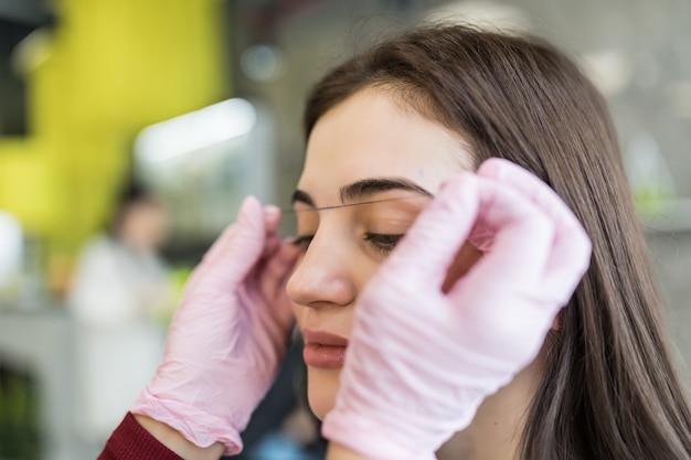 Meisterin in weißen Handschuhen überprüft die Kontur der Augenbrauen