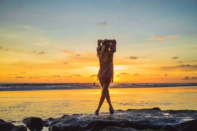 Kostenloses Foto menschen am strand bei sonnenuntergang. das mädchen springt gegen den hintergrund der untergehenden sonne.