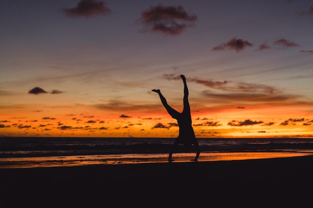 Menschen am Ufer des Ozeans bei Sonnenuntergang. Mann springt gegen den Hintergrund der untergehenden Sonne