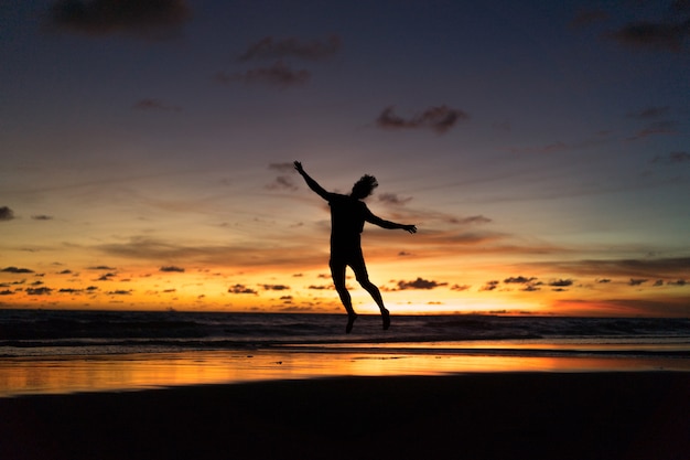 Menschen am Ufer des Ozeans bei Sonnenuntergang. Mann springt